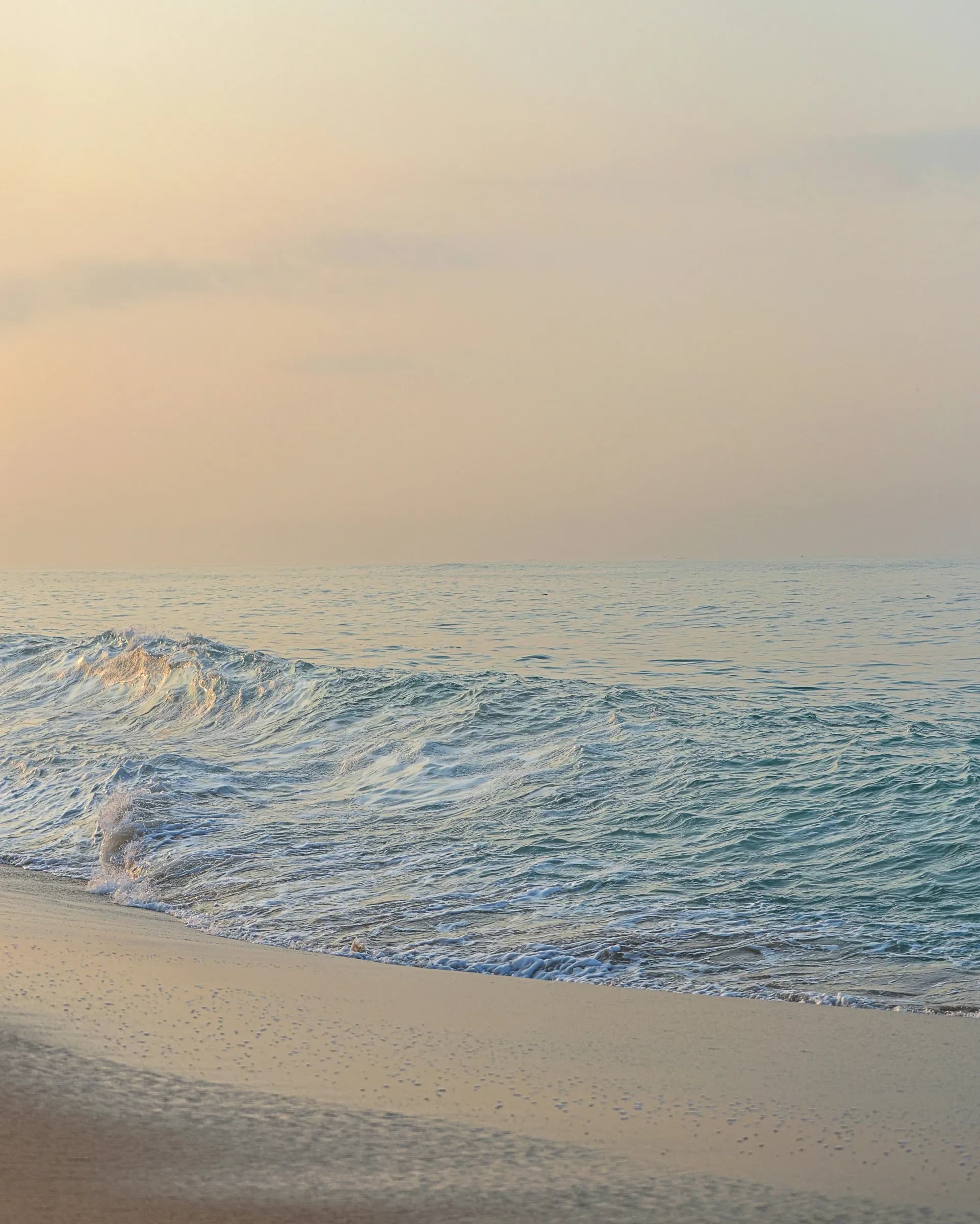 Gentle waves meeting a sandy beach under a soft, hazy sky
